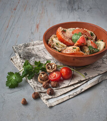 food photography of summer healthy vegetable vegetarian tomato salad side view with onions, parsley and nuts in a brown ceramic bowl on a gray concrete texture background