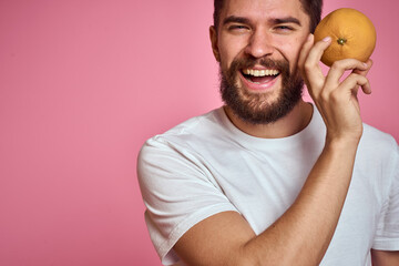 Young man with orange on a pink background in a white t-shirt emotions fun gesticulating with model...