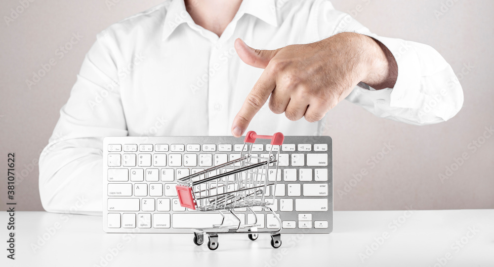Poster online shopping concept. man pointing on empty shopping cart with keyboard on background