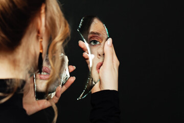 Serious woman looking at broken self-image mirror on black background