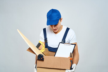 man in working uniform with a box in his hands tools loader delivery light background