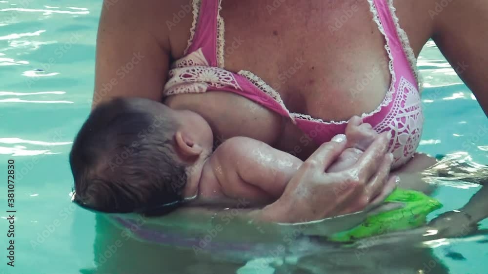 Wall mural Young baby sucking milk from mother's breast in the pool