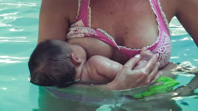 Young baby sucking milk from mother's breast in the pool