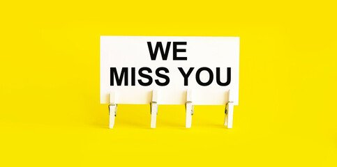 text WE MISS YOU on white short note paper yellow background
