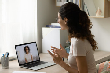 Happy Caucasian young woman sit at desk at home talk speak on video call on laptop with biracial friend. Smiling millennial female have webcam online lesson or conference with tutor on computer.