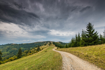 Curving dirt road on the top of the mountains in the Carpathian mountains, Romania, dramatic storm clouds in the background.
