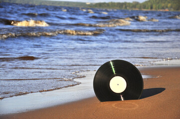 Vinyl record on the sea sand against the surf.