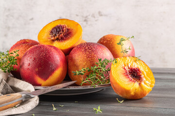 Ripe peaches with thyme leaves in a plate on a wooden board on a background