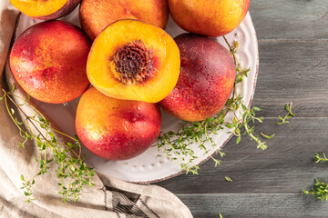 Ripe peaches with thyme leaves in a plate on a wooden board on a background