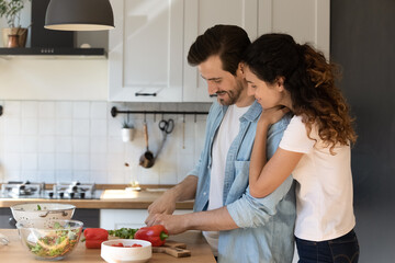 Obraz na płótnie Canvas Happy Caucasian couple tenants enjoy lazy morning in modern kitchen cooking together. Smiling loving young man and woman renters preparing healthy delicious vegetarian food at new own home.