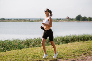Young sporty woman running in the park by the pond on a warm summer day