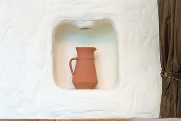 A brown jug in a niche on a white wall.