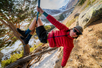 A man tightrope walker hangs on a slackline in a cap and sunglasses in the afternoon on a sunny...