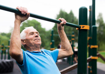 Naklejka premium mature cheerful pensioner man doing physical exercises on sports equipped playground