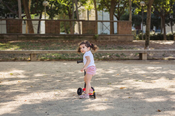 little girl plays in park with toy scooter