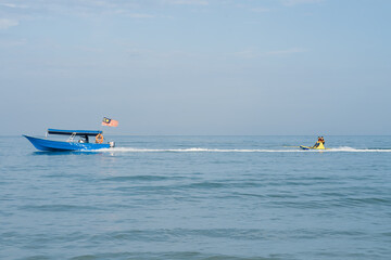 Boat with Malaysian flag is pulling children standing on the floating water raft in the sea.