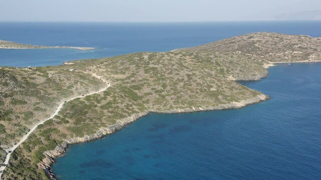 Aerial drone view of a dry, yellow landscape along the Greek coastline in Summer (Kolokytha, Elounda, Crete)