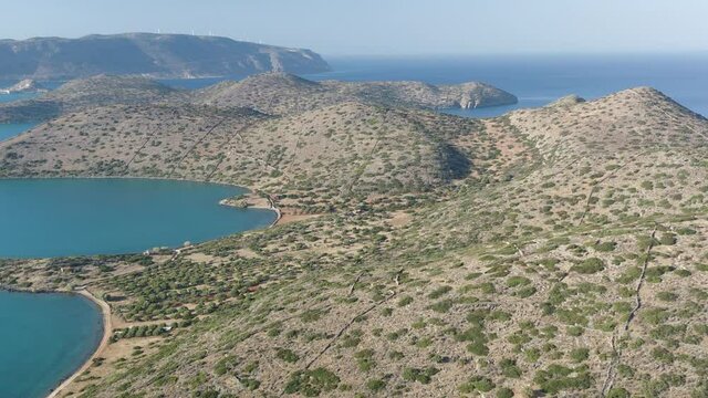 Aerial drone view of a dry, yellow landscape along the Greek coastline in Summer (Kolokytha, Elounda, Crete)
