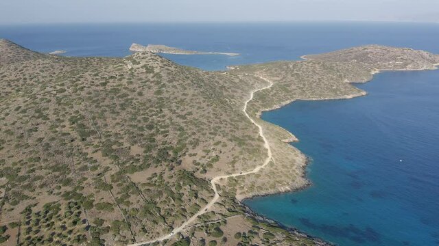 Aerial drone view of a dry, yellow landscape along the Greek coastline in Summer (Kolokytha, Elounda, Crete)