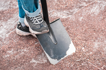Womens feet in sneakers stick bayonet shovel into the ground.