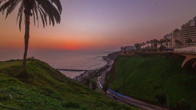 Aerial sunset view of Lima's Coastline in the neighborhood of Miraflores timelapse with orange light, Lima, Peru. Road with traffic and beach with ocean. Palm near Love park