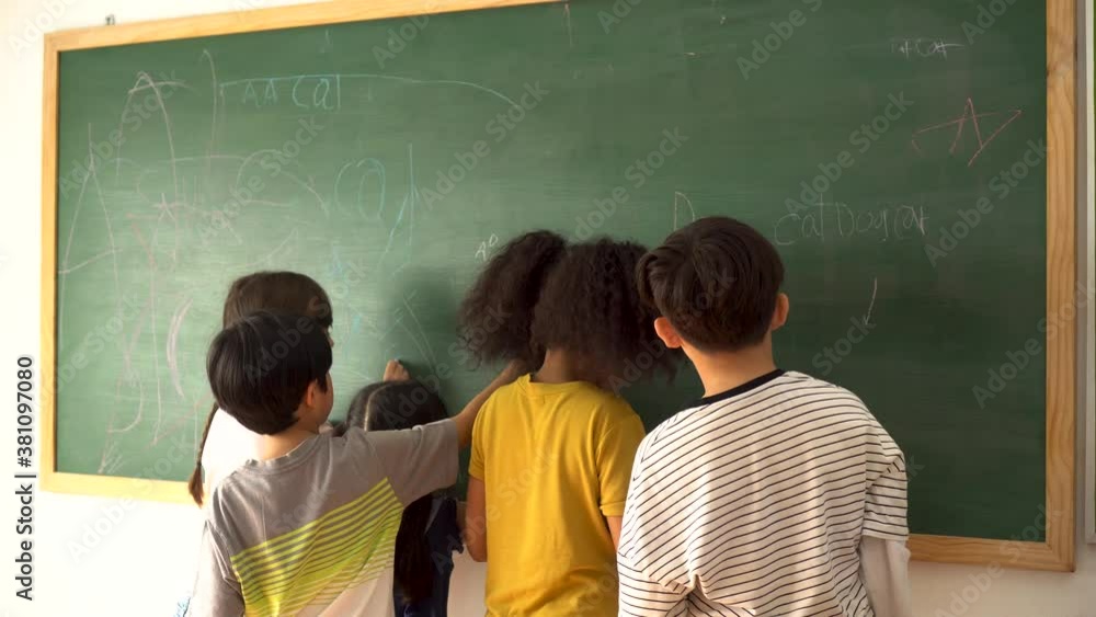 Wall mural Multiethnic group of school children using chalkboard in school classroom, education, learning, fun. Diverse elementary students writing on blackboard