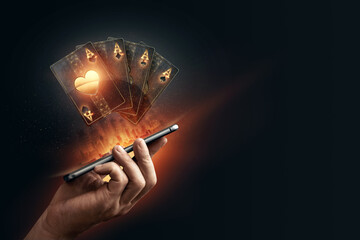 In the hands of a smartphone with playing cards, black-gold background. Concept of online gambling,...