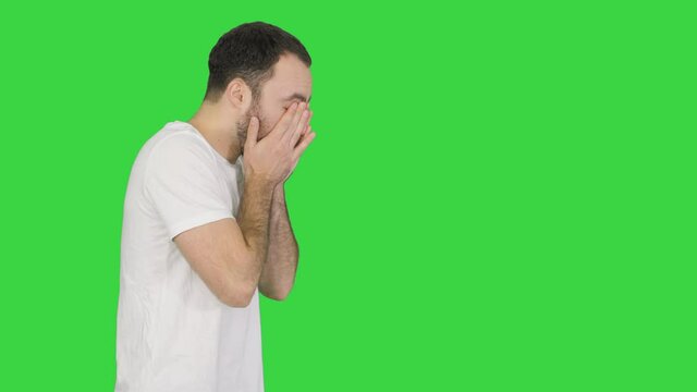 Sleepy male in white t-shirt yawning and rubbing eyes while walking on a Green Screen, Chroma Key.