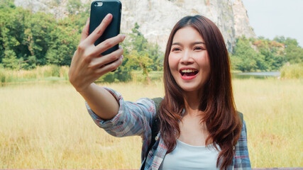 Cheerful young traveler Asian lady with backpack recording video vlog live streaming on phone...