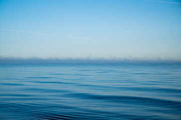 ocean with light waves in bright blue as a conceptual background with a horizon shrouded in light fog and plenty of space for text or design