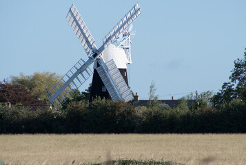 Fototapeta premium A windmill in a Fenland village with farmland in the foreground and the village beyond. 