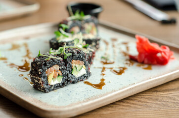 Set of rolls of black rice, fish and philadelphia cream cheese, sesame seeds, on a white plate, poured with unagi sauce and microgreen sprouts, side view