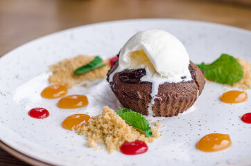 Delicious sweet chocolate fondant with drops of colorful jam and a scoop of melted ice cream, on a white plate in a cafe
