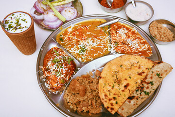 Top view of traditional Rajasthani thali Jaipur,  India. Missi and jowar ki roti with side dishes dal fry, gatta masala, baati ball, raita, churma sweet and lassi. Indian vegetarian food.