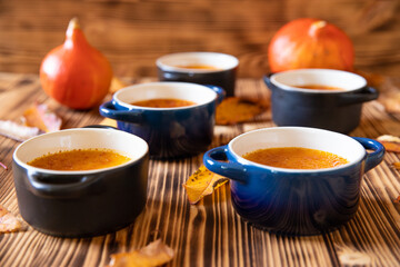orange Creme Brulee aus Kürbis vom Hokkaido mit  karamellisierter Zuckerkruste in Förmchen auf einem braunen Holztisch mit Laubblättern im Herbst