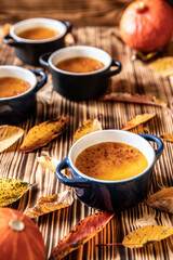 orange Creme Brulee aus Kürbis vom Hokkaido mit  karamellisierter Zuckerkruste in Förmchen auf einem braunen Holztisch mit Laubblättern im Herbst