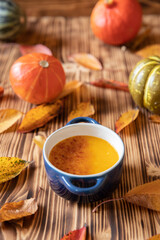 orange Creme Brulee aus Kürbis vom Hokkaido mit  karamellisierter Zuckerkruste in Förmchen auf einem braunen Holztisch mit Laubblättern im Herbst