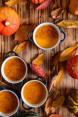 orange Creme Brulee aus Kürbis vom Hokkaido mit  karamellisierter Zuckerkruste in Förmchen auf einem braunen Holztisch mit Laubblättern im Herbst