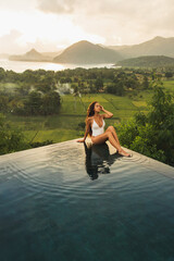 Dream journey in Asia. Woman sitting on edge luxury infinity pool an enjoying amazing mountain,...