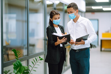 Naklejka na ściany i meble Business colleagues with face mask discussing together work issues at office. Teamwork during pandemic in quarantine city. Covid-19.