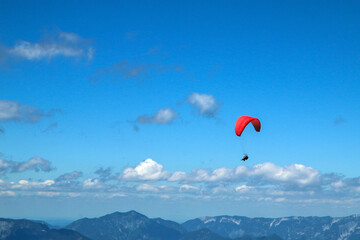 The paraglides are flying above the mountains high in the blue sky and enjoying the view. 