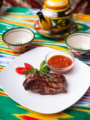beef steak with tomato sauce, tomatoes and herbs in oriental style on a table with a teapot and a cup for tea.