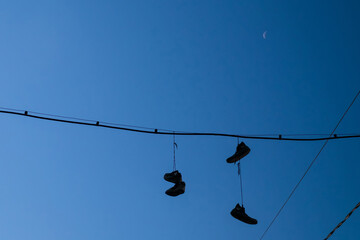 Obraz premium Silhouettes of shoes hanging on wires against the blue sky. Selective focus