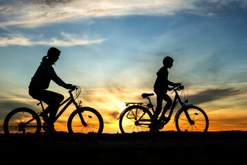 Fototapeta na wymiar Boy , kid 10 years old, and girl riding bikes in countryside in amazing colorful cloudy night sky background, silhouette of riding persons at sunset in nature 