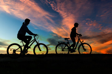 Boy , kid 10 years old, and girl riding bikes in countryside in amazing colorful cloudy night sky...