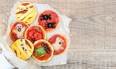 Halloween mini pizza with cheese, olives and ketchup.  Funny food for children. Decorated mummy, ghost, spiders, zombie. Background of an old wood