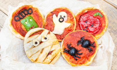 Halloween mini pizza with cheese, olives and ketchup.  Funny food for children. Decorated mummy, ghost, spiders, zombie. Background of an old wood