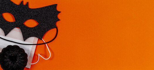 Black halloween eye mask, little black pumpkin and medical protective face mask on orange background