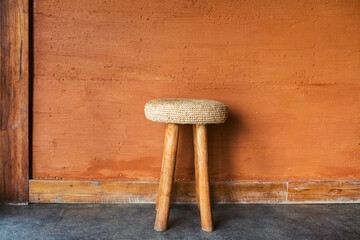 Handmade wooden chair with wicker straw pillow on background of red terracotta wall with decorative plaster. Moroccan rustic interior and furniture design.