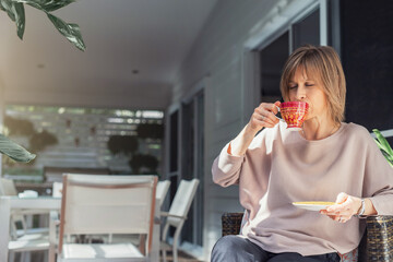 Naklejka premium Middle-aged woman drinking coffee or tea enjoying on the balcony.